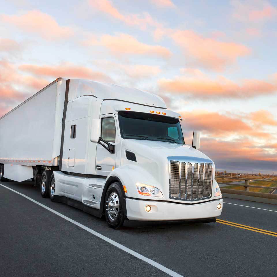 Cropped white semi-truck driving on a two lane highway at sunrise