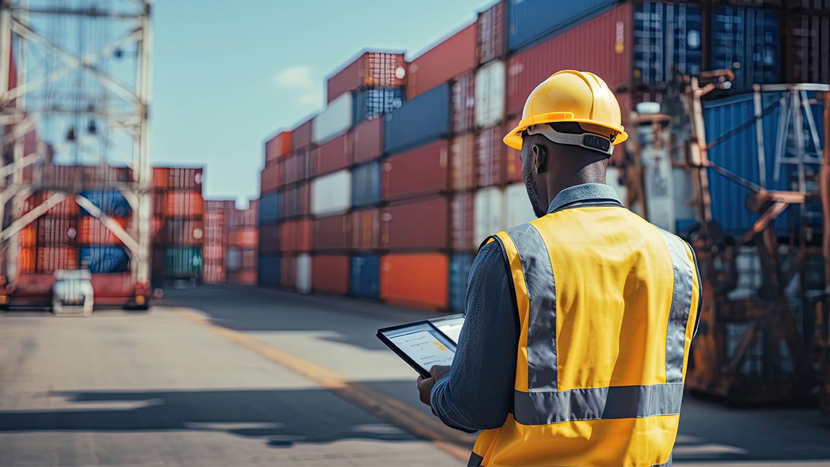 Worker on tablet, stacks of shipping containers surround them.